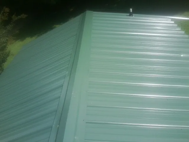 New green metal panels meeting at the ridge of a roof — Flat Roof Repair work by our crew in Belvidere