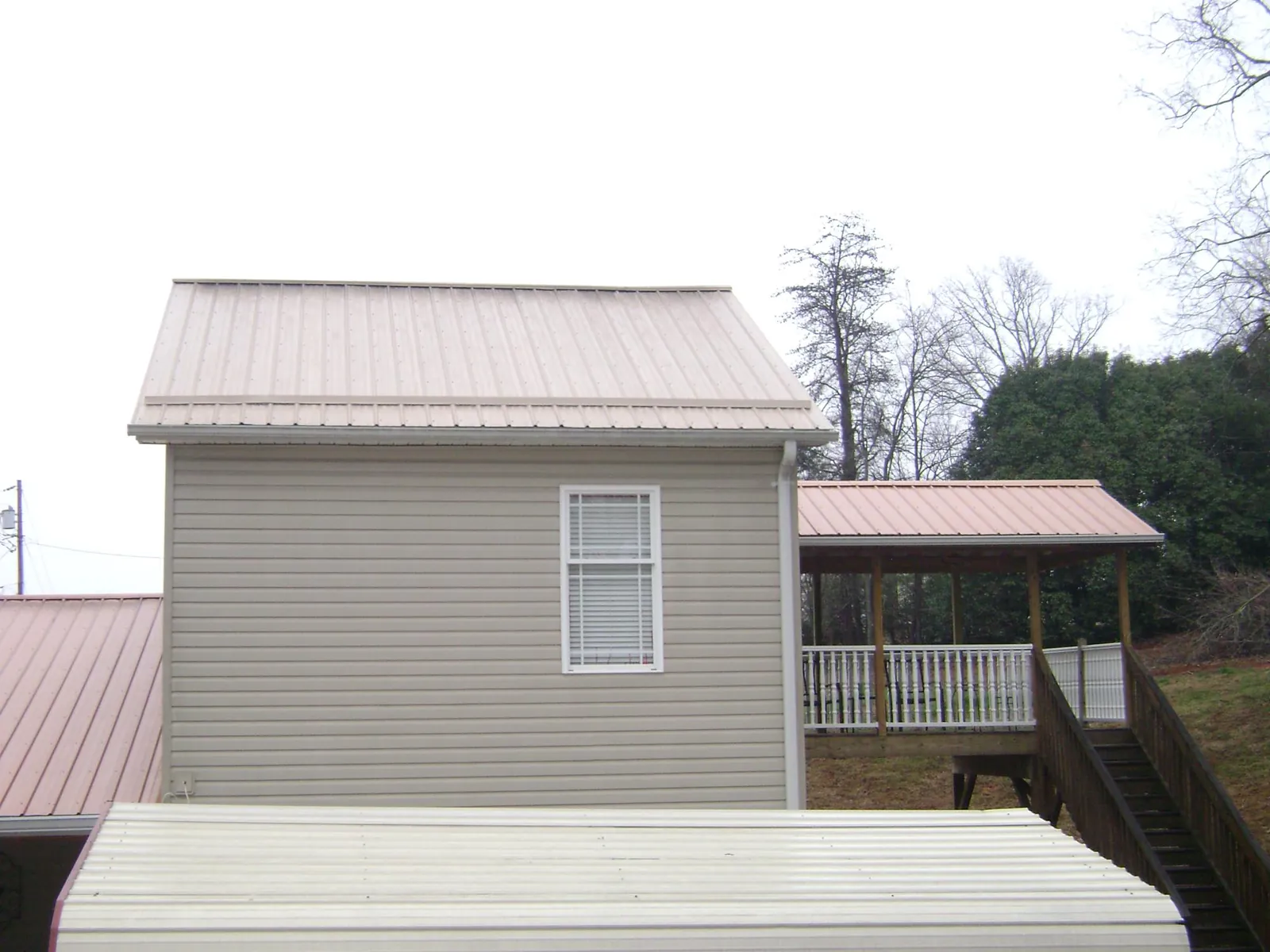 Tan metal roofs on a two story addition and attached porch, from a Roof Replacement job in Belvidere